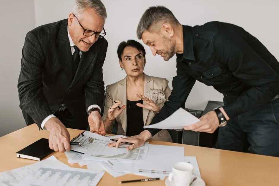 Three professionals in discussion at an office table, analysing documents together